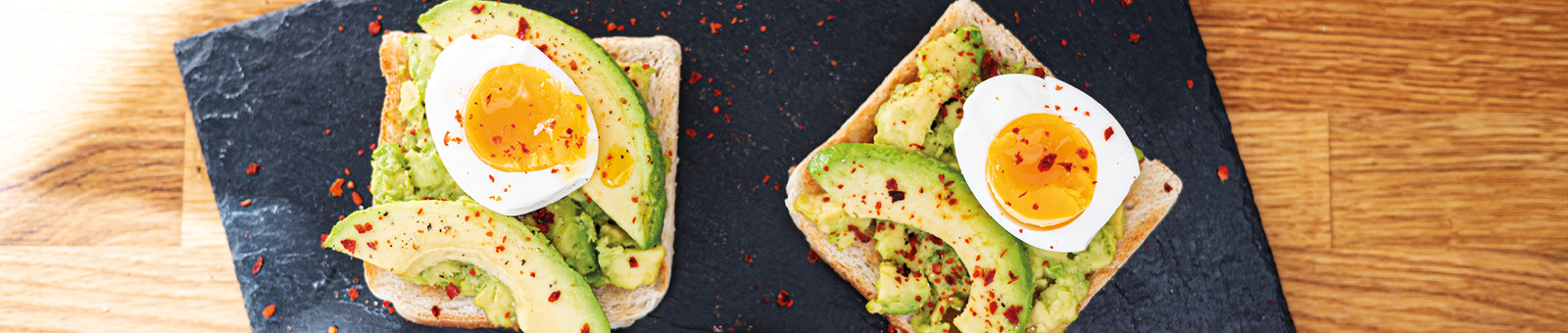 Das Bild zeigt eine Schieferplatte mit Avocado Toasts und Ei.