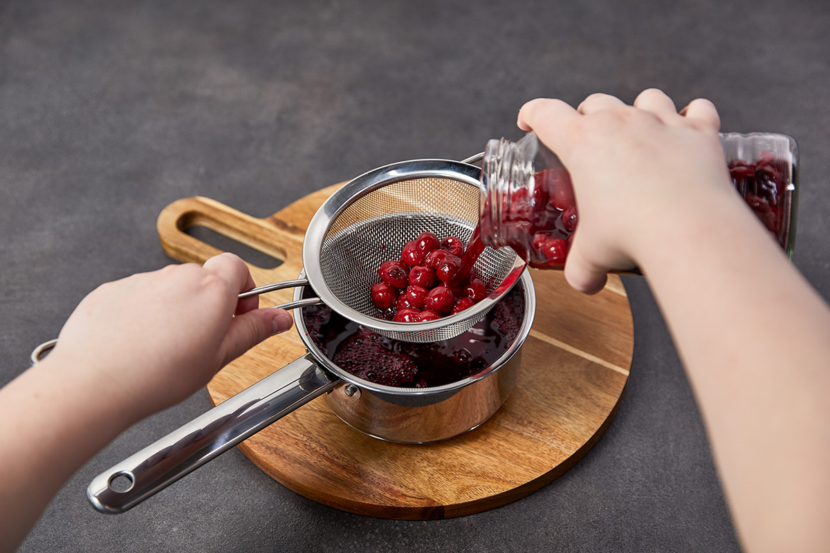 Das Bild zeigt wie die Kirschen mithilfe eines Siebes vom Kirschsaft getrennt werden.